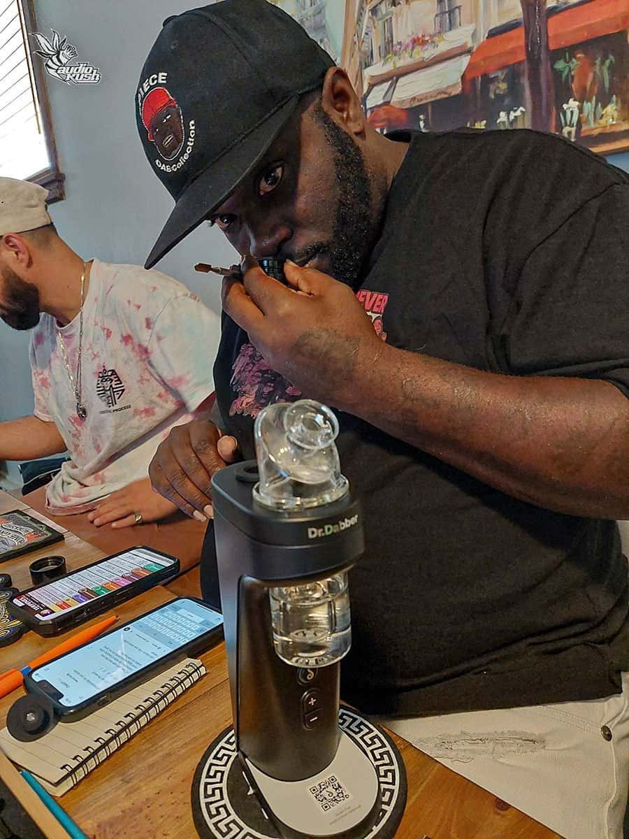 Highly detailed cannabis dab rig, vaporizer with glass water pipe, and concentrates, at a busy music and vaping event.