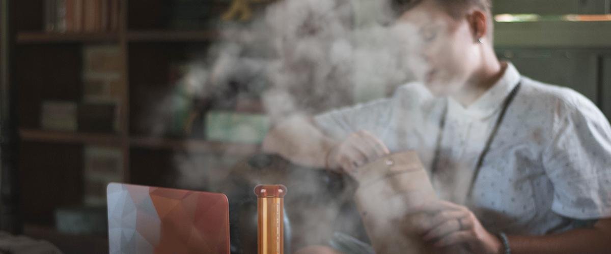 Vape enthusiast vaping indoors with a colorful vaporizer at home, creating thick vapor clouds.