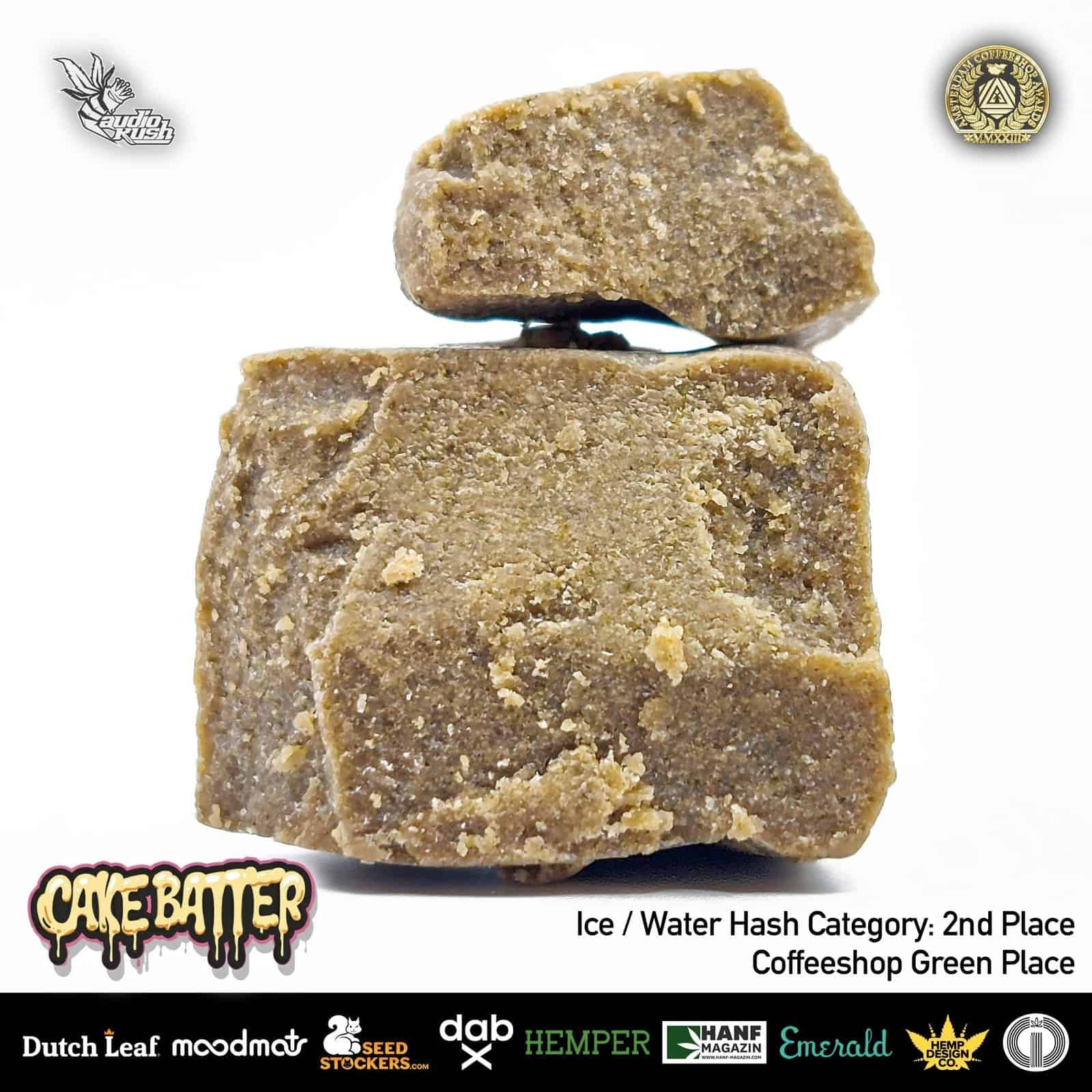 1. Dark brown hash cubes stacked, close-up of cannabis concentrates used in edibles and dabbing, with branding logos visible in the background.