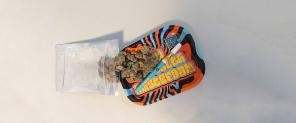 Colorful psychedelic packaging with cannabis buds, a pre-rolled joint, and a grinder on a plain background for legal recreational or medical marijuana use.