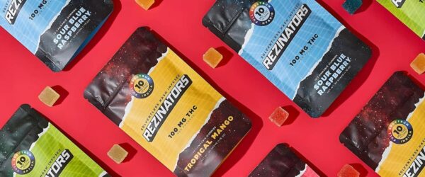 Vape product packaging with colorful galaxy-themed labels on a red background, featuring cannabis gummy ingredients and labeling, with small sugar cubes nearby.