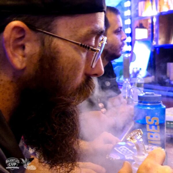 Man with beard and glasses smokes dabs from a glass rig
